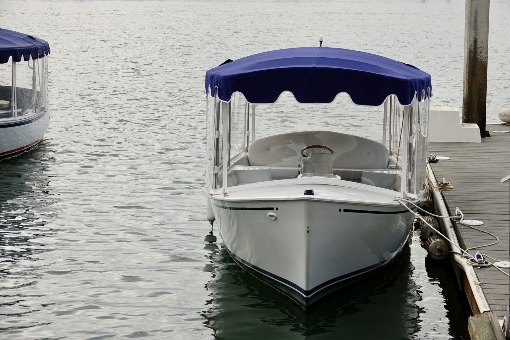 A white boat with a blue canopy is docked at a wooden pier on calm water.